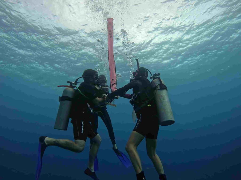 PADI Open Water Diver students practice how to launch a surface marker buoy (SMB). A SMB is used by scuba divers, at the end of a line from the diver, intended to indicate the diver's position to people at the surface while the diver is underwater.