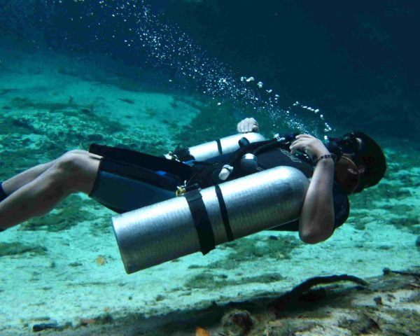 An open water diver performing neutral buoyancy drills while in sidemount configuration